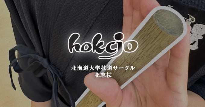 木製の「杖」を構えた人物と「hokcjo」ロゴ
